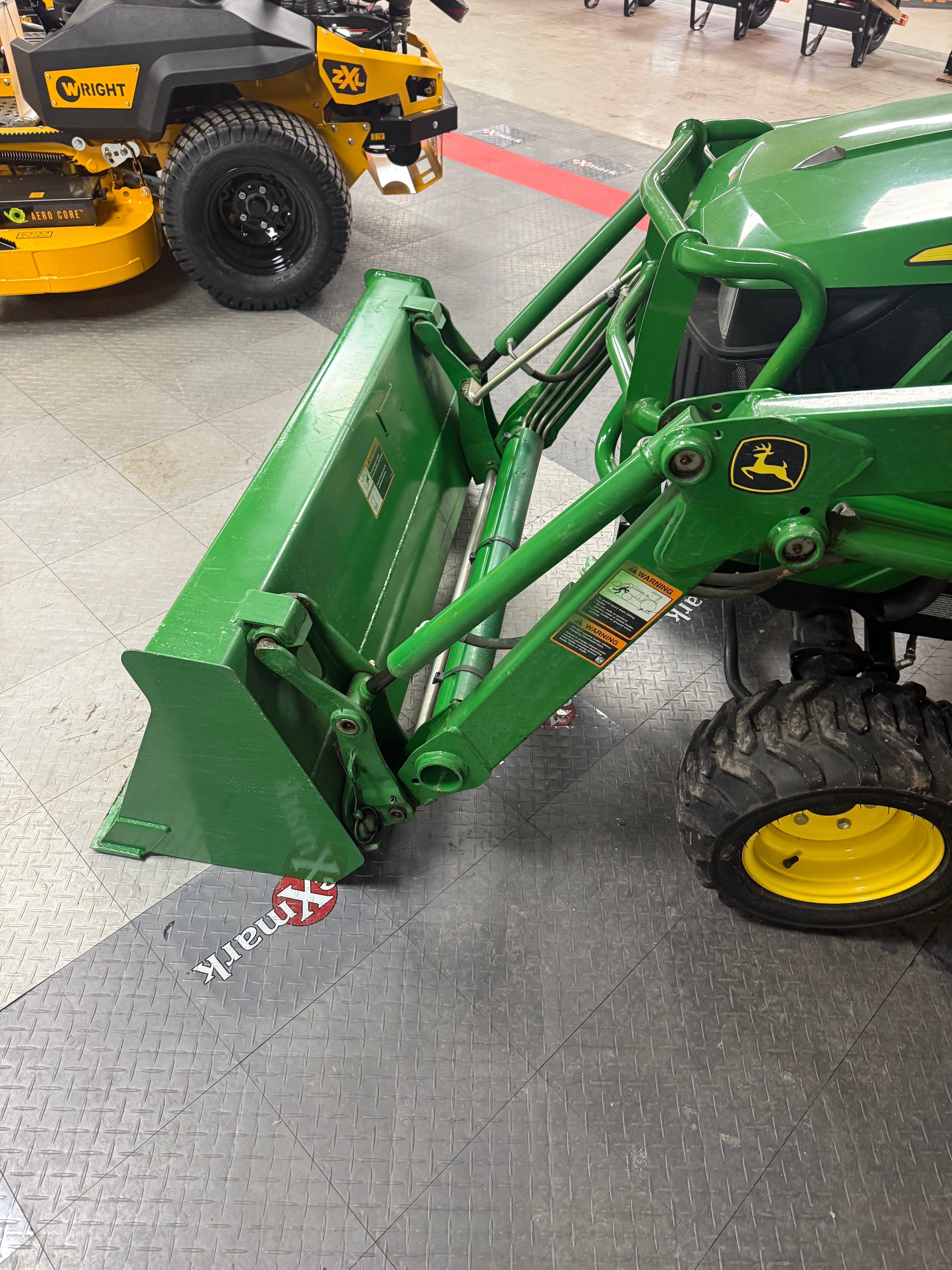Green tractor attachment on a tiled floor with 'Xmark' branding.