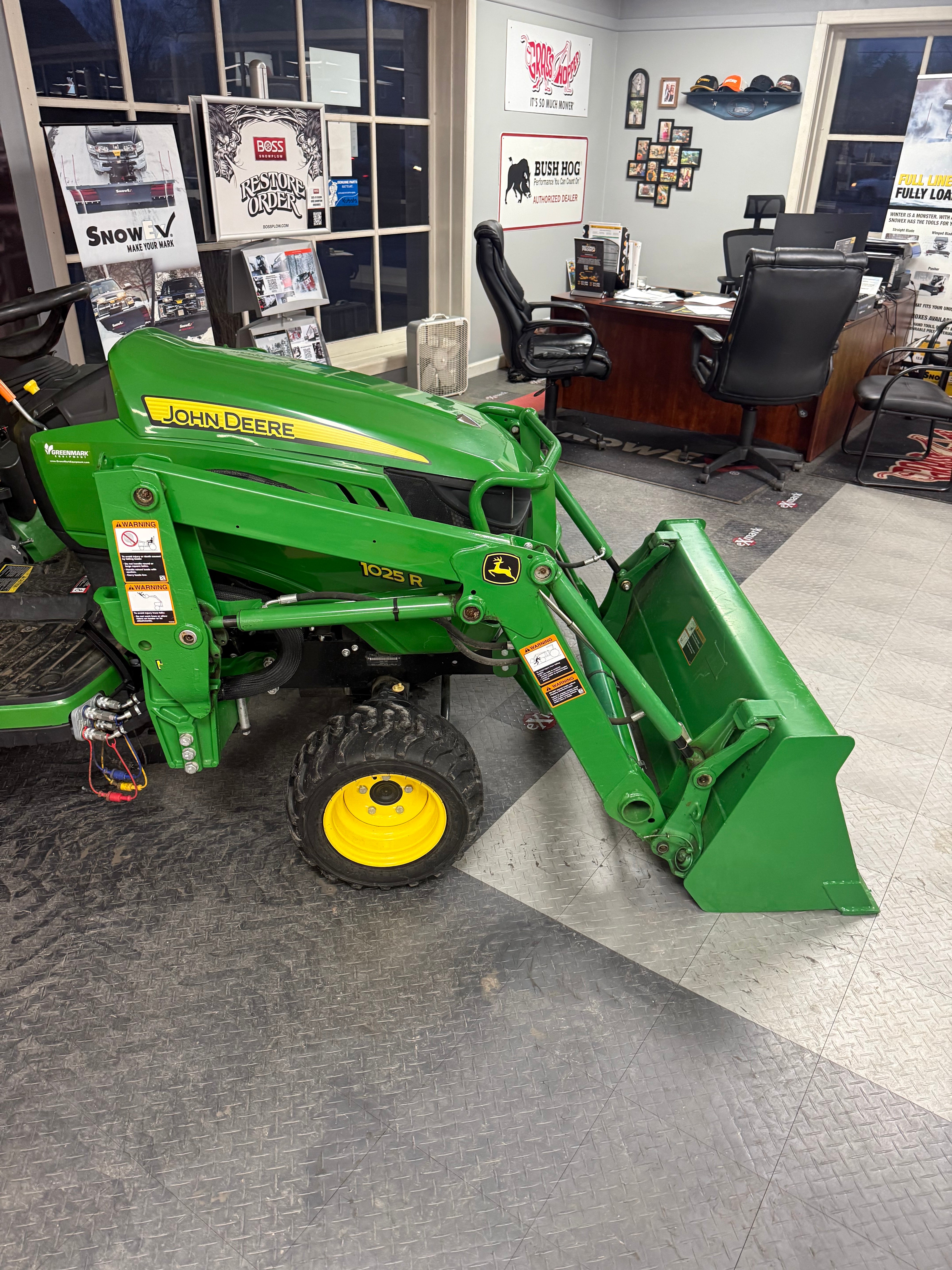 Green tractor with a front loader attachment on a concrete floor.