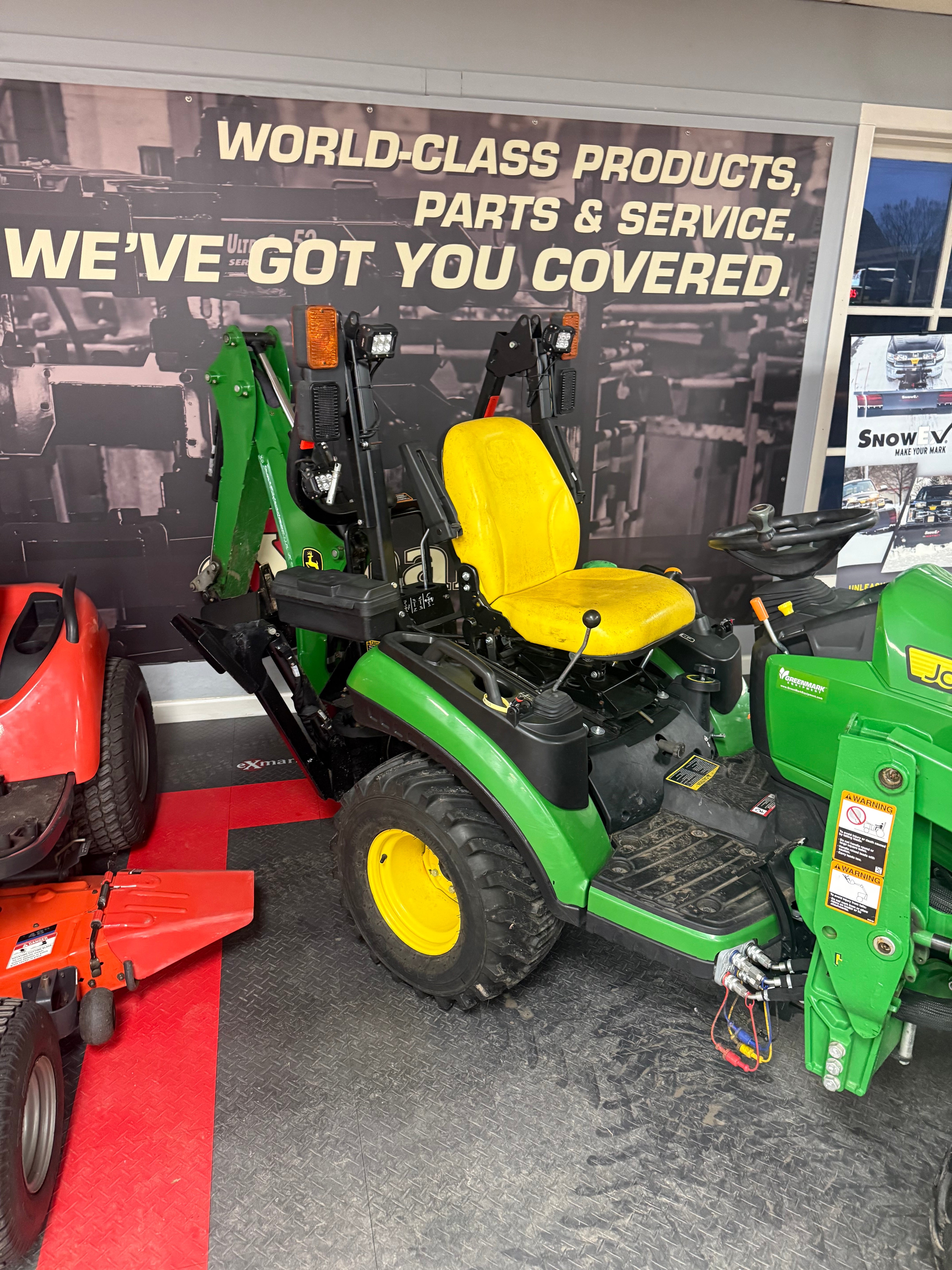 Green and yellow lawn tractor on display with a promotional poster in the background.