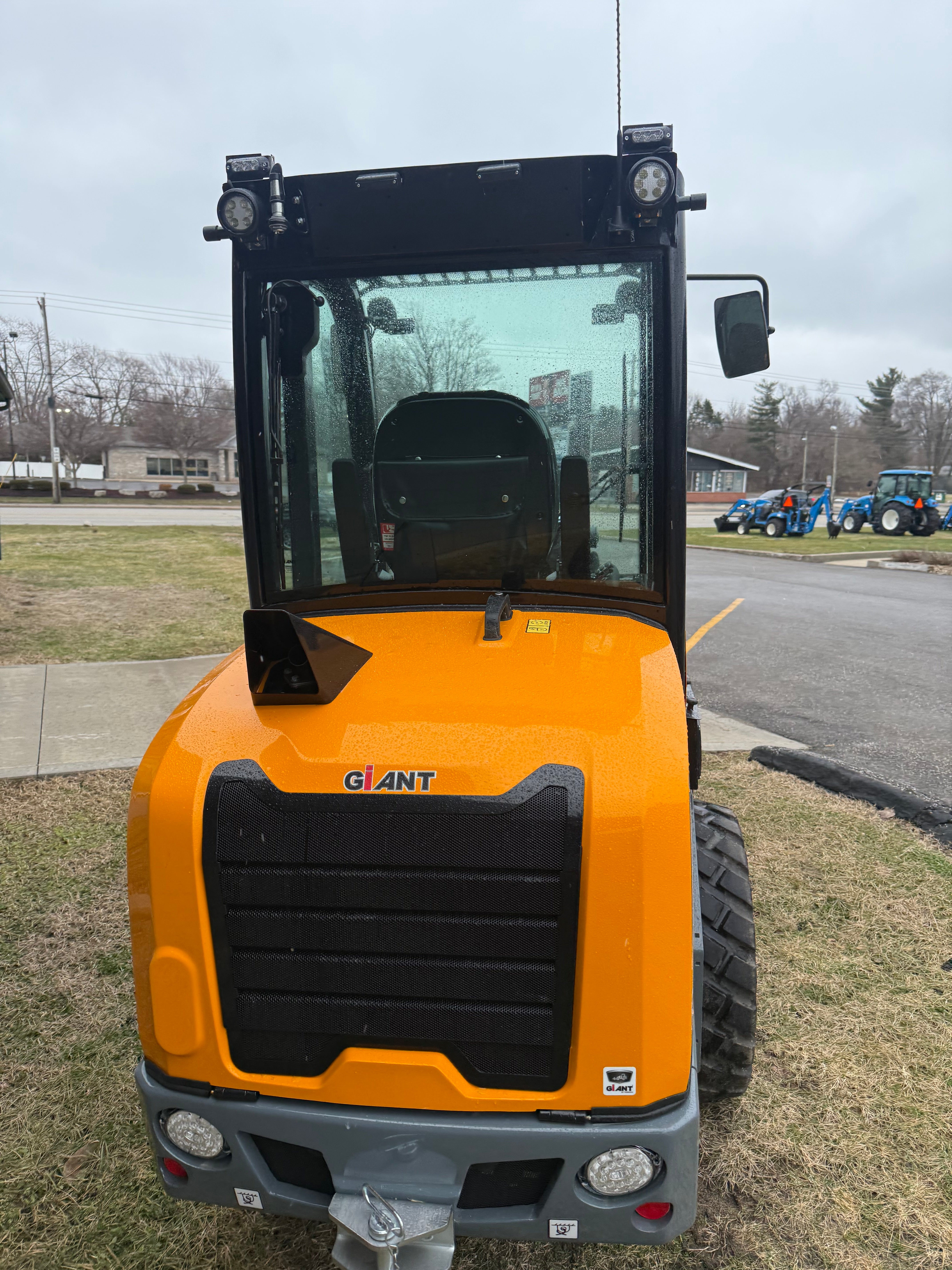 Yellow forklift on a grassy area with a road and trees in the background