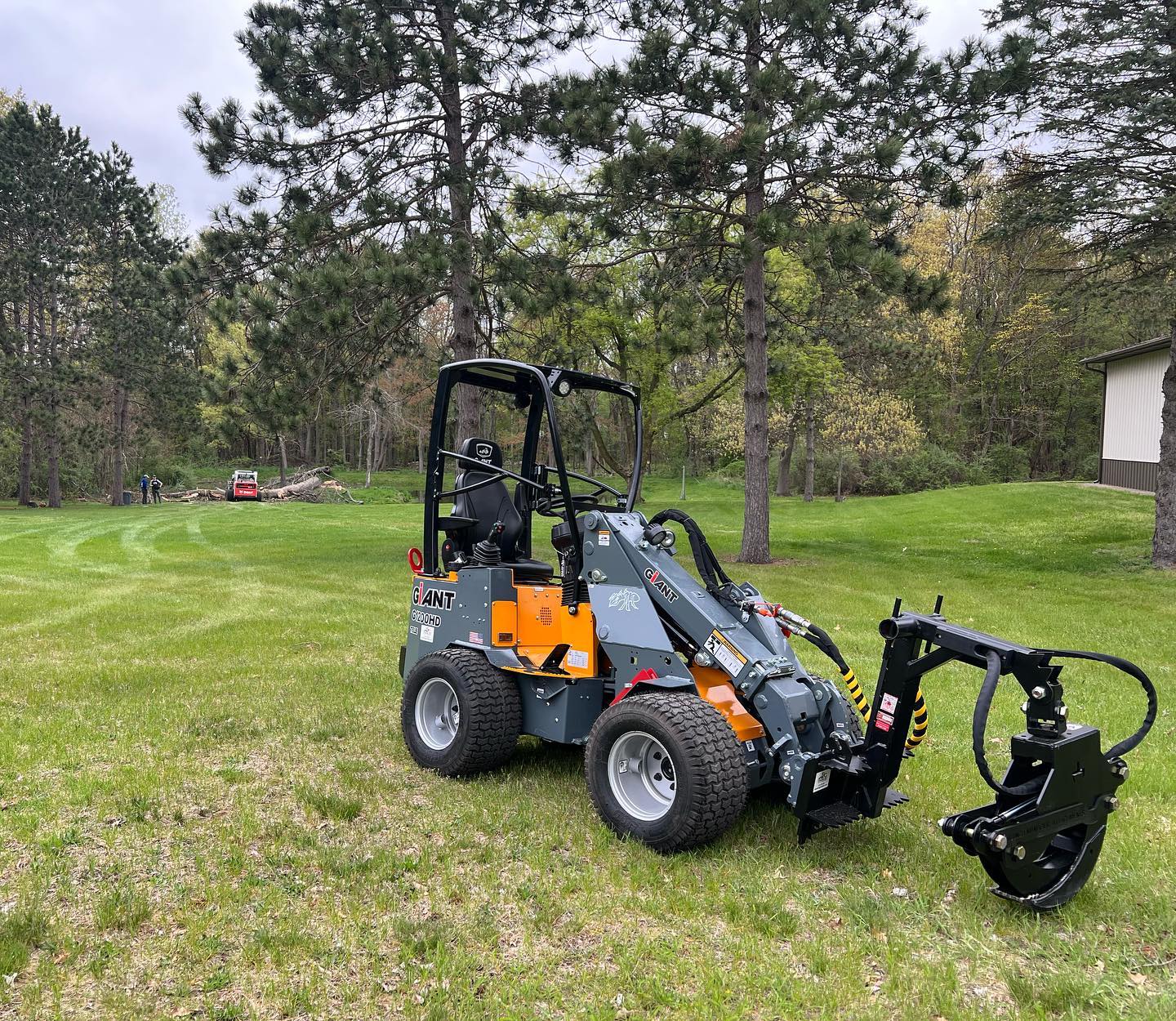 Small backhoe loader on a grassy field with trees in the background