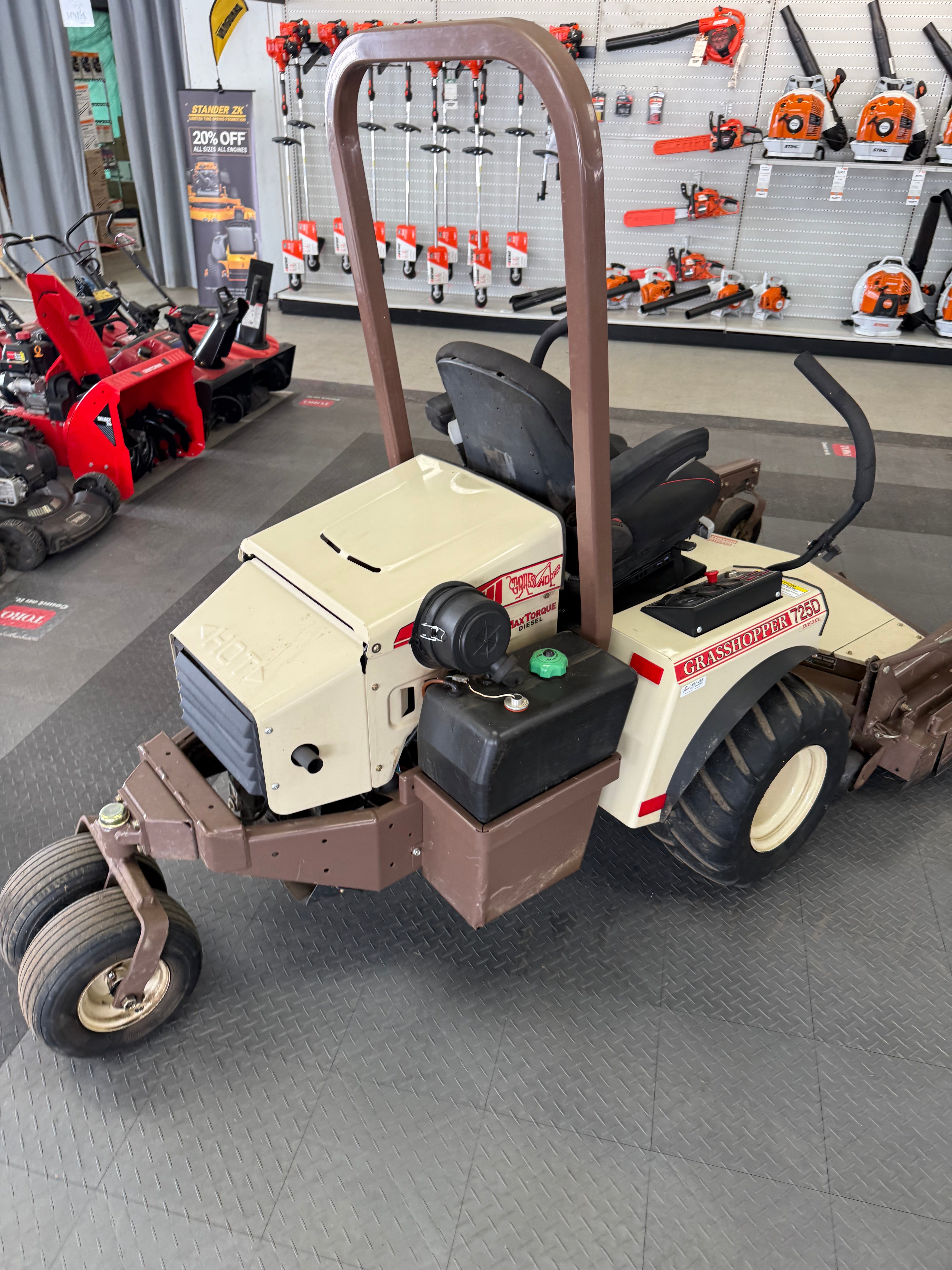 Small forklift or lifting device in a workshop setting with tools and equipment in the background.