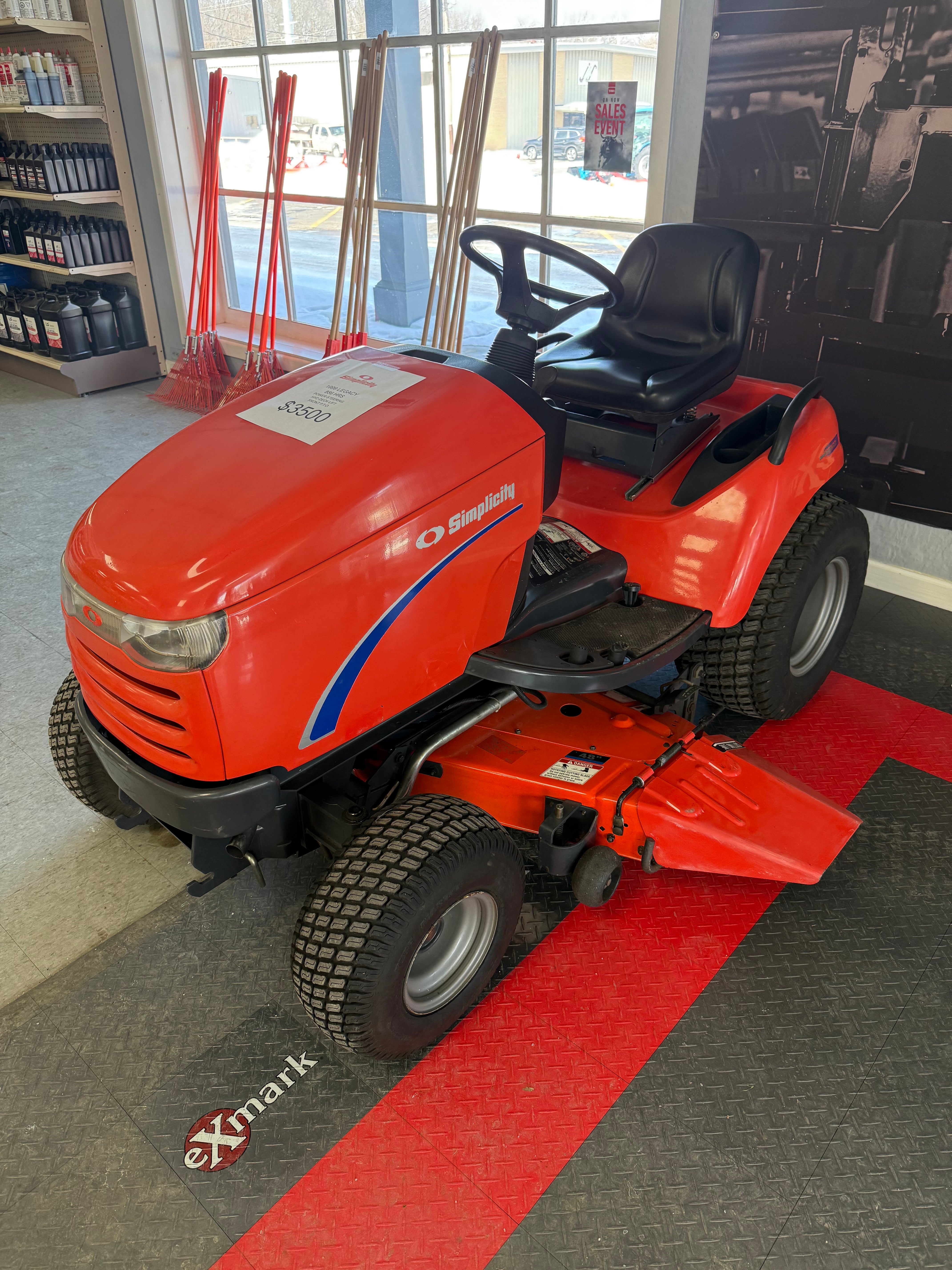 Red lawn mower on display in a showroom with a red carpet.