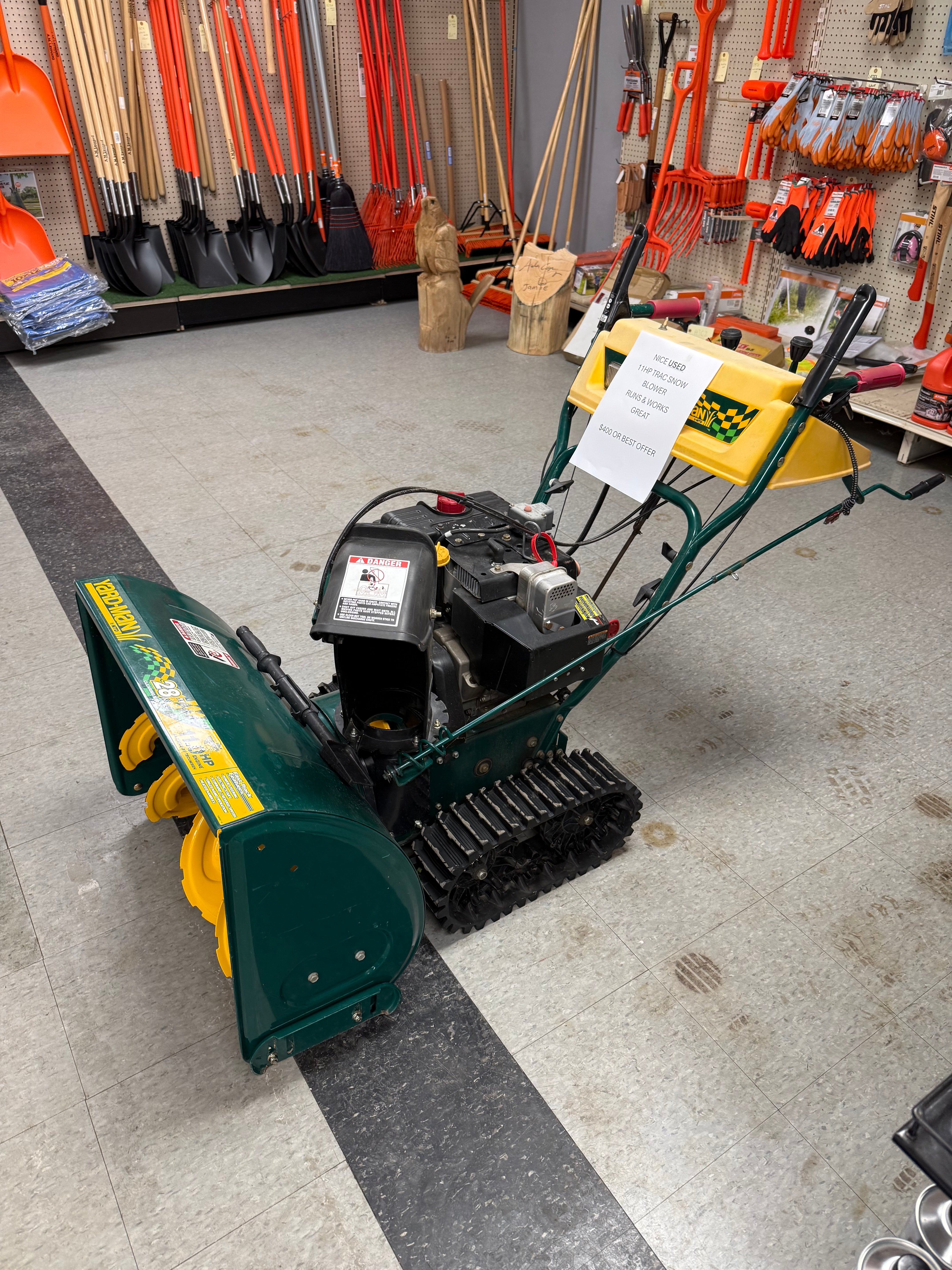 Green and yellow snow blower on a concrete floor with tools in the background